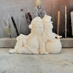Könnte beinhalten: Eine weiße Keramikfigur von Weihnachtsmann, der mit einem Schneemann sitzt. Der Weihnachtsmann trägt einen Hut und hat einen Bart. Der Schneemann trägt einen Hut und einen Schal.