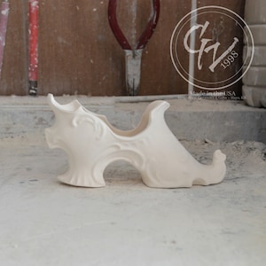 May include: White ceramic wine bottle holder shaped like a shoe with intricate details. Made in the USA by Grapevine Ceramics & Gifts, Hays, KS.