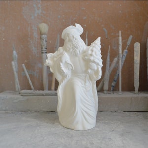 May include: White ceramic figurine of Santa Claus holding a Christmas tree. The figurine is unpainted and ready to be decorated.