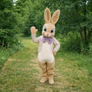 May include: A person in a full-body bunny costume with large ears, a purple bow tie, and a plaid jacket, standing on a grassy path. The costume is primarily tan and cream-colored, with large, expressive eyes. The background is a green, tree-lined path.