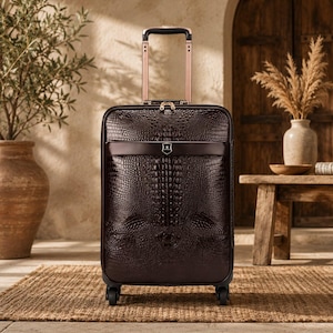 May include: A dark brown rolling suitcase featuring a textured crocodile skin pattern. The luggage has a retractable rose gold handle, four spinner wheels, and a horizontal band across the upper front section with a small centred metallic emblem.