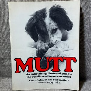 May include: A book cover with a black and white puppy illustration. The title "MUTT" is in red, with the text "An entertaining, illustrated guide to the world's most famous underdog" below. The book is a guide.