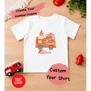 Peut inclure: T-shirt blanc avec un dessin de camion de pompiers rouge et orange avec un ours en peluche au volant. Le chiffre 6 est au-dessus du camion et le nom "William" en dessous. Le texte sur le t-shirt dit "Choisissez votre numéro/nom" et "Personnalisez votre chemise."