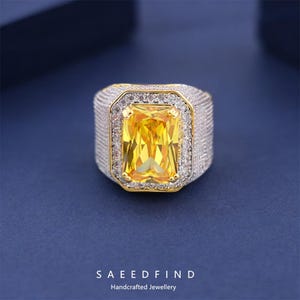 May include: A rectangular yellow gemstone ring with a gold and silver setting. The ring features a large, vibrant yellow center stone surrounded by smaller, clear stones. The band is silver with a textured design. The brand name "SAEEDFIND" is at the bottom.
