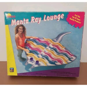 May include: A boxed Manta Ray Lounge inflatable pool float. The float is shaped like a manta ray with colorful stripes in shades of blue, yellow, pink, and purple. The box features the text "Manta Ray Lounge" and "Feel The Fun Of Sunco Quality Products!"