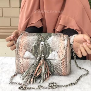 Könnte beinhalten: Rechteckige Handtasche mit Schlangenmuster in Grün-, Rosa- und Grautönen. Die Tasche hat einen silbernen Kettenriemen und einen dekorativen Quastenanhänger. Der Text "SUNUPLEATHER" ist oben sichtbar.