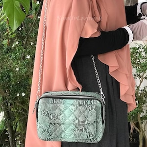 Könnte beinhalten: Rechteckige, mintgrüne Umhängetasche mit Schlangenmuster. Die Tasche hat einen silbernen Kettenriemen und eine kleine Vordertasche. Die Tasche ist aus Leder und hat einen Reißverschluss. Die Tasche ist ein Modeaccessoire.