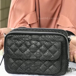 Könnte beinhalten: Schwarze Umhängetasche mit einem Steppmuster und einer Vordertasche. Die Tasche hat einen silbernen Reißverschluss und einen Kettenriemen. Die Tasche besteht aus einem strukturierten Material, möglicherweise Leder. Der Text "SUMUPLEATHER" ist sichtbar.