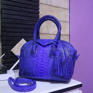 May include: A striking blue handbag with a snakeskin texture. It has a top handle, a detachable shoulder strap, and a tassel. The bag is displayed on a white surface.