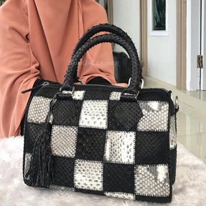 May include: A black and white checkered handbag with braided handles and a tassel. The bag is made of a textured material, possibly leather, and has a zipper closure. The bag is approximately 30 cm wide.
