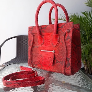 May include: Red handbag with a snakeskin pattern, featuring two top handles and a detachable shoulder strap. The bag has a front zip pocket and a silver-toned zip. The brand name "SUMU LEATHER" is visible on the front.