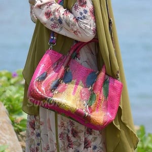 May include: A bright pink tote bag with a colourful, abstract pattern. The bag is rectangular and structured. The word "SUMU" is visible on the bag. The bag is carried over the shoulder.