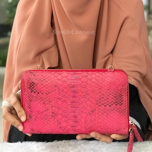 Könnte beinhalten: Eine leuchtend pinkfarbene, rechteckige Clutch mit Schlangenmuster. Die Clutch hat einen Reißverschluss und eine kleine Handschlaufe. Der Text "SumUpLeather" ist im Hintergrund sichtbar.