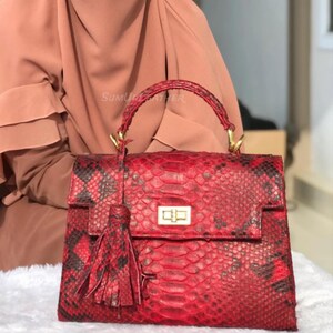 May include: A white ceramic mug with a black handle and the text "But First, Coffee" in a bold, black font. The mug is set against a blurred background, suggesting a cosy setting.