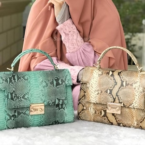 Könnte beinhalten: Zwei Lederhandtaschen mit Schlangenmuster. Eine ist türkis und die andere ist beige und braun. Beide haben goldfarbene Verschlüsse und Griffe. Die Taschen sind rechteckig mit einem Klappenverschluss.