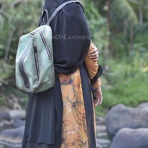 May include: A light green backpack with a textured snakeskin pattern and a dark gray vertical center stripe. The bag features two prominent vertical zippered compartments with black pulls and thin black shoulder straps. The text UPLEATHER is visible.