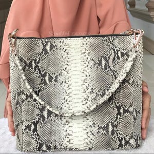 Könnte beinhalten: Ein Set aus drei Keramikbechern mit gesprenkelter, matter Oberfläche. Die Becher sind in Creme-, Hellgrau- und Dunkelgrautönen gehalten. Jeder Becher hat ein schlichtes, minimalistisches Design.