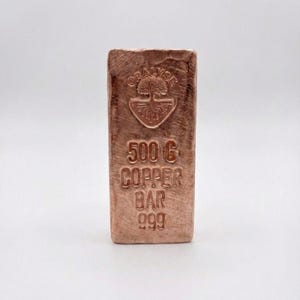 Könnte beinhalten: Kupferbarren mit dem Text "ORALYSE" über einem Baumlogo und "500 G COPPER BAR 999" auf der Vorderseite. Der Barren hat eine rechteckige Form und eine strukturierte Oberfläche. Der Kupferbarren wiegt 500 Gramm.