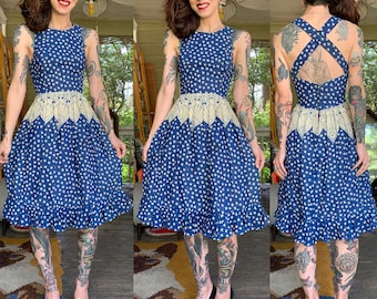 Puede incluir: Un vestido floral azul y blanco con un ribete de encaje blanco y una espalda cruzada. El vestido tiene un corpiño ajustado y una falda completa.