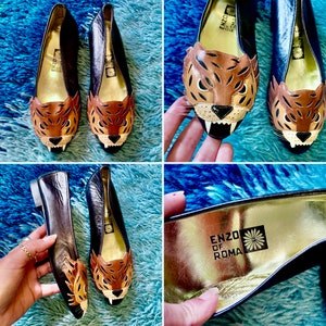 May include: A pair of black leather flats with a brown and black leopard print design. The shoes have a pointed toe and a gold insole with the text "ENZO di ROMA".