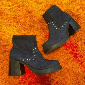 May include: A pair of denim ankle boots with silver studs and chunky heels. The boots are on a fuzzy orange rug.