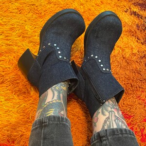 May include: A pair of dark blue denim ankle boots with silver studs. The boots have a chunky heel and a zipper on the side.