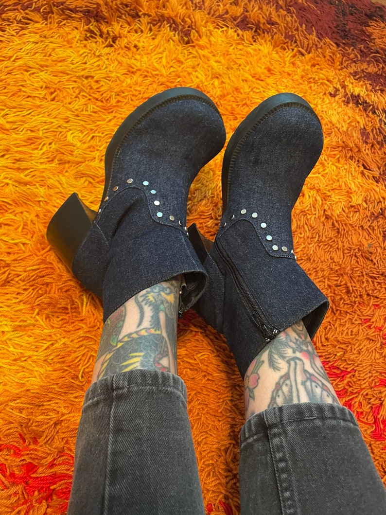 May include: A pair of dark blue denim ankle boots with silver studs. The boots have a chunky heel and a zipper on the side.