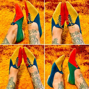 May include: A pair of colorful shoes with red, yellow, and blue suede panels. The shoes have a pointed toe and lace-up closure. The shoes are worn by a person with tattoos on their legs.