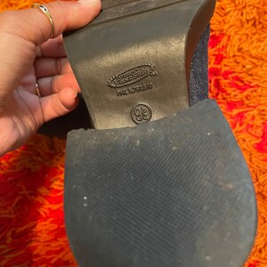 May include: Close-up of the bottom of a dark blue denim boot with a black rubber sole. The sole has the text "Guess Base Side" and "PAT. 5,787,510" printed on it.