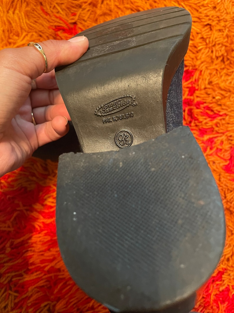 May include: Close-up of the bottom of a dark blue denim boot with a black rubber sole. The sole has the text "Guess Base Side" and "PAT. 5,787,510" printed on it.