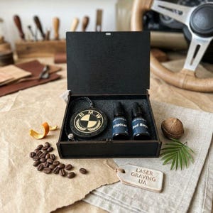 May include: A black wooden box set containing a car air freshener with a BMW logo, two small bottles, and a tag that reads "LASER GRAVING UA". The set includes coffee beans, an orange peel, and a coconut.