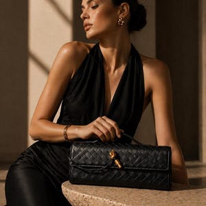 May include: A black woven leather handbag featuring a rectangular silhouette, a top handle, and a gold-toned knot detail on the front flap. The bag has a structured design with a consistent grid-like texture across the entire exterior surface.