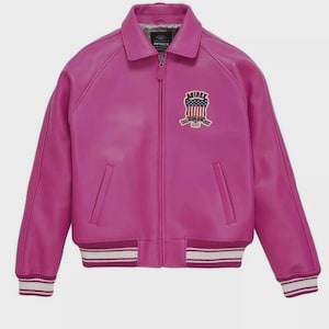 Pode incluir: Casaco de couro f&uacute;csia com fecho de correr, gola e punhos canelados. Um patch "AVIREX" com um design de bandeira americana adorna o peito. Os punhos e a bainha apresentam riscas brancas e bord&ocirc;.