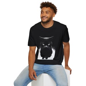 May include: Black t-shirt featuring a striking black and white graphic of a cat with glowing eyes. The cat's intense gaze is the focal point of the design. The shirt is a casual wear item.