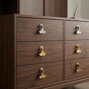 Puede incluir: Cómoda de madera marrón oscuro con seis cajones. Los tiradores de los cajones tienen forma de hojas de ginkgo, con acabados plateados y dorados. La cómoda es de madera y tiene una superficie lisa y pulida.