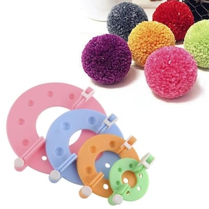 May include: A collection of colorful pom-poms in various colors, including purple, pink, orange, green, red, and gray.  Below are pink, blue, orange, and green pom-pom makers. These craft tools are designed to create fluffy pom-poms for various DIY projects.