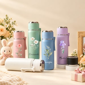 Könnte beinhalten: Eine Sammlung von fünf zylindrischen Wasserflaschen aus Edelstahl in den Pastellfarben Rosa, Mintgrün, Hellblau, Lavendel und Weiß. Jede Flasche hat einen Metalldeckel, eine seitliche Trageschlaufe und ein Blumenmotiv. Zwei Flaschen sind mit den Namen Corisande und Greta personalisiert.