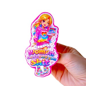 May include: A colorful sticker featuring a cartoon girl with blonde hair, a pink sweater, and a rainbow heart design. The sticker includes the text "Women don't owe you shit" in a playful font. The girl is holding a laptop with a rainbow on the screen.