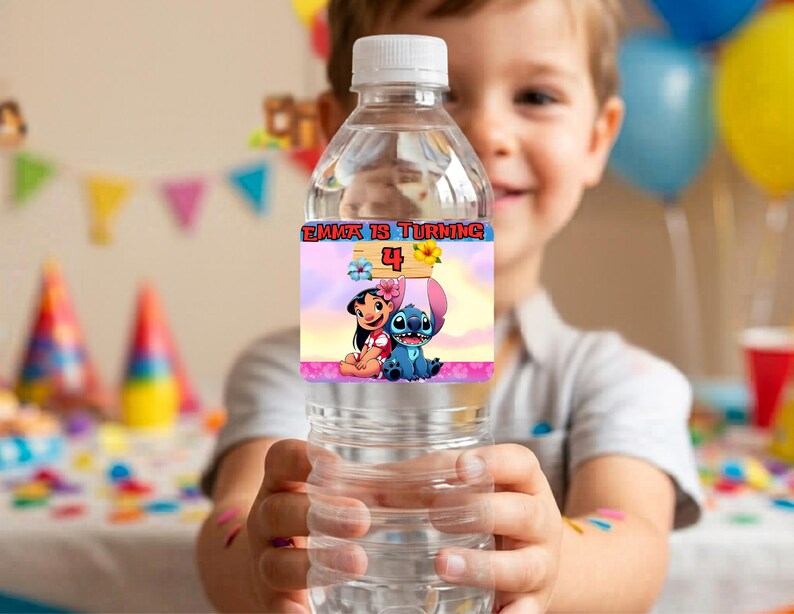 A smiling boy holding a clear water bottle wrapped in a custom Lilo and Stitch birthday party label. The label reads 'Emma is turning 4' with a tropical pink and blue Hawaiian theme. The background is a brightly lit, blurred kids birthday party scene featuring colorful balloons, party hats, and festive pennant banners, showcasing the printable party decor in use.