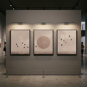 Puede incluir: Tres impresiones artísticas enmarcadas con bordes negros se exhiben en una pared gris. Cada impresión presenta una paleta de colores apagados con una bandada de pájaros en vuelo o un círculo grande. Encima de cada impresión hay una lámpara negra.
