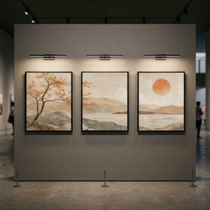 Può includere: Tre dipinti di paesaggi incorniciati con cornici nere sono esposti su un muro grigio. Ogni dipinto presenta una scena diversa con colori tenui, tra cui un albero, montagne e un tramonto. Sopra ogni dipinto c'è un apparecchio di illuminazione nero.