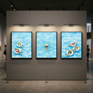 May include: Three framed art prints depicting people in a pool with white inflatable rings and hats. The water is a light blue with ripples. The prints are displayed in a gallery setting with spotlights.