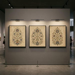 May include: Three rectangular framed wall art pieces displayed in a row, each featuring a symmetrical botanical illustration of a flowering plant in muted blue, red, and green tones on a textured beige background, illuminated by individual lights.