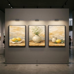 Könnte beinhalten: Drei gerahmte Aquarellmalereien, die in einer Galerie ausgestellt sind. Jedes zeigt ein Stillleben: Zitronen, eine Vase mit weißen Blumen und einen Krug mit einer Zitrone. Das Kunstwerk ist vor einem neutralen Hintergrund mit warmen Tönen.