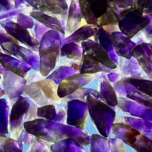 May include: A collection of amethyst crystals in various shapes and sizes. The crystals display shades of purple, lavender, and white, with some areas appearing translucent. The arrangement creates a textured, gemstone-like appearance.