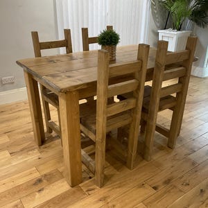 May include: A wooden dining table and four chairs, all made from light-coloured wood. The table has a rectangular top and is surrounded by four matching chairs. A small potted plant sits on the table. The table is approximately 122 cm long.