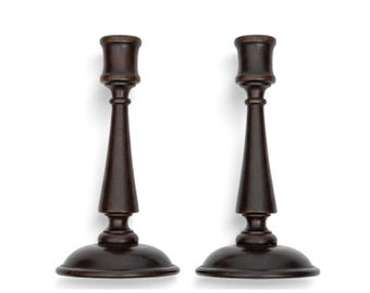 May include: A pair of dark brown wooden candle holders featuring a smooth, tapered stem design with a wide, circular base and a cylindrical top cup for holding a candle. The finish is matte and uniform, showcasing the natural wood grain texture.
