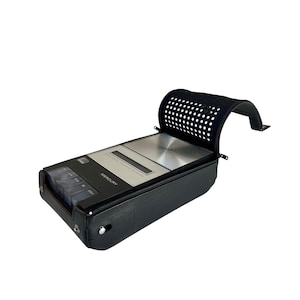 Puede incluir: Un grabador de cintas de casete Mercury negro vintage con una placa frontal plateada y una cubierta negra perforada. El grabador tiene una funda de cuero y una serie de botones para reproducir, rebobinar y detener. El dispositivo está diseñado para reproducir cintas de audio.