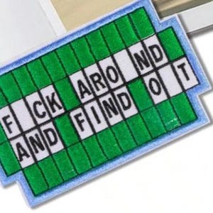 May include: A rectangular embroidered patch featuring a green grid pattern resembling a crossword puzzle. The white squares contain black capital letters spelling out the phrase FUCK AROUND AND FIND OUT, with a light blue border surrounding the design.