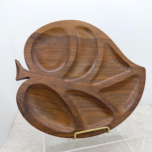 May include: A wooden leaf-shaped serving tray with multiple compartments. The tray is made of dark brown wood and has a natural wood grain pattern. It features a small handle and is designed for serving snacks or appetizers.